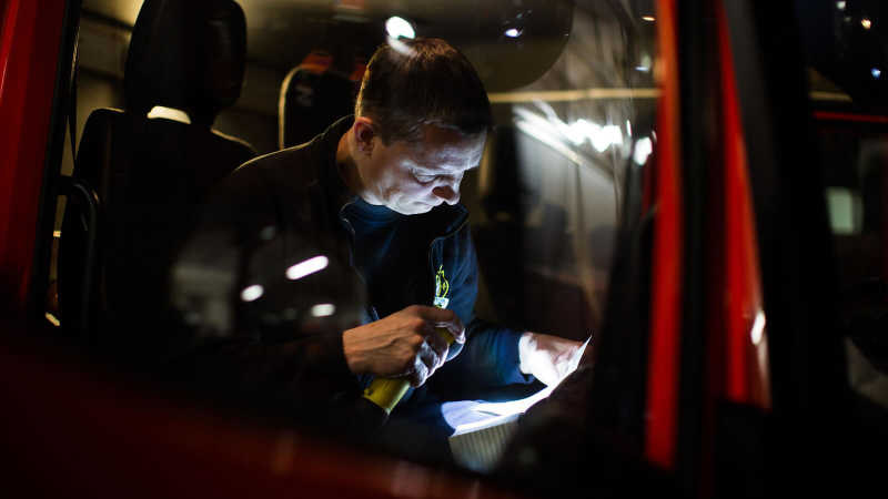 Das Bild zeigt einen Feuerwehrmann, der die Fahrzeugpapiere einer Drehleiter prüft.