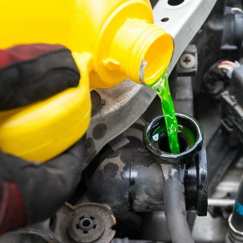 Eine grünliche Flüssigkeit wird aus einem gelben Kanister in eine Öffnung eines Pkw-Motors geschüttet.