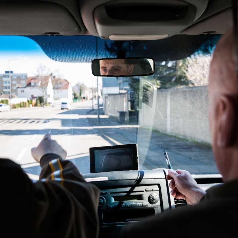 Das Bild zeigt eine Prüfungssituation im Fahrzeug während der Fahrt. Der Blick des Prüfenden und des Prüflings sind nach vorne gerichtet.
