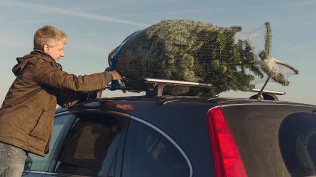 Ein Mann sichert einen Tannenbaum auf seinem Autodach.