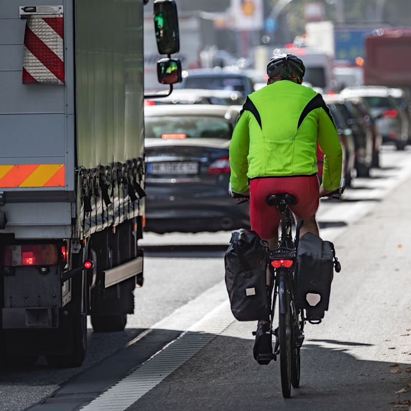Radfahrer im toten Winkel eines Lkw. Tipps zur Unfallprävention und sicheren Teilnahme am Straßenverkehr.