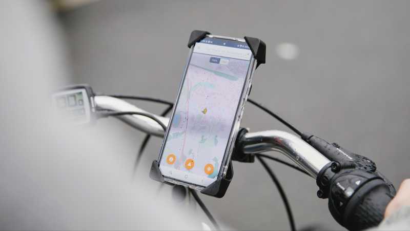 An einem Fahrradlenker ist ein Handy montiert. Auf dem Display des Handys ist ein digitaler Stadtplan zu sehen. 