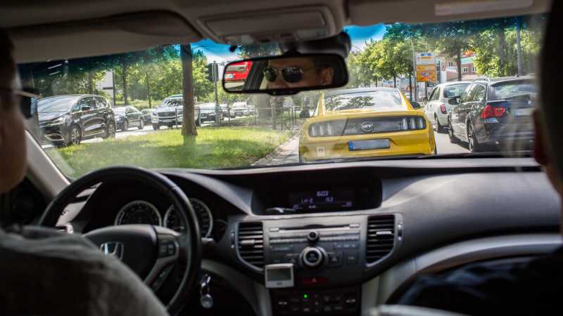 Das Bild zeigt zwei SoKo-Beamte im Einsatz. Sie verfolgen unauffällig einen gelben Sportwagen in der Innenstadt.