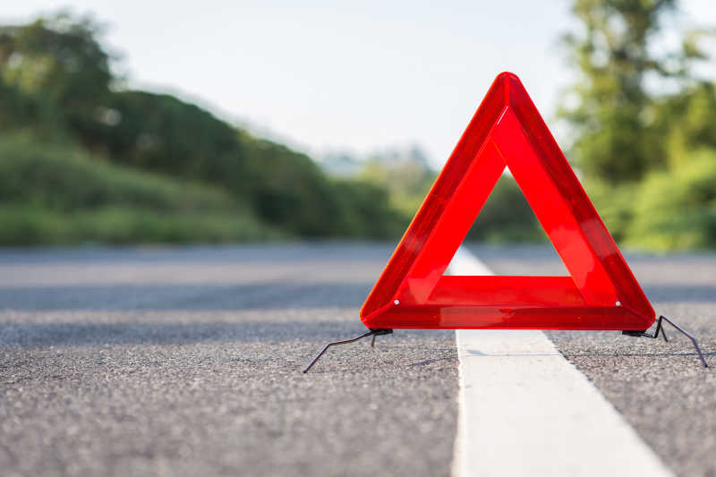 Ein rotes Warndreieck, welches bei Unfällen aufgestellt werden muss, steht auf einer Landstraße.