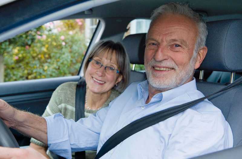 Ein älteres Ehepaar sitzt im Auto und lächelt in die Kamera.