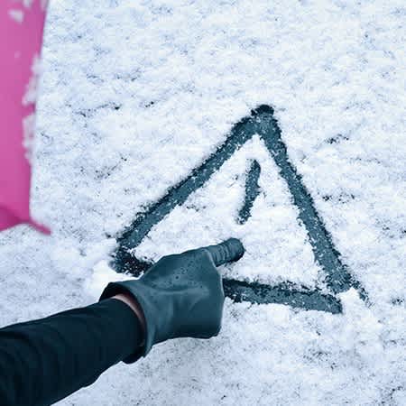 Jemand malt ein Ausrufezeichen in den Schnee auf der Windschutzscheibe eines Autos.