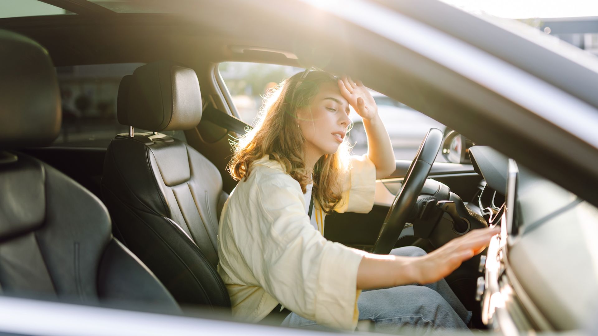 Eine junge Autofahrerin leidet erschöpft unter extremer Hitze im Auto am Steuer ihres Fahrzeugs an einem heißen, sonnigen Sommertag.