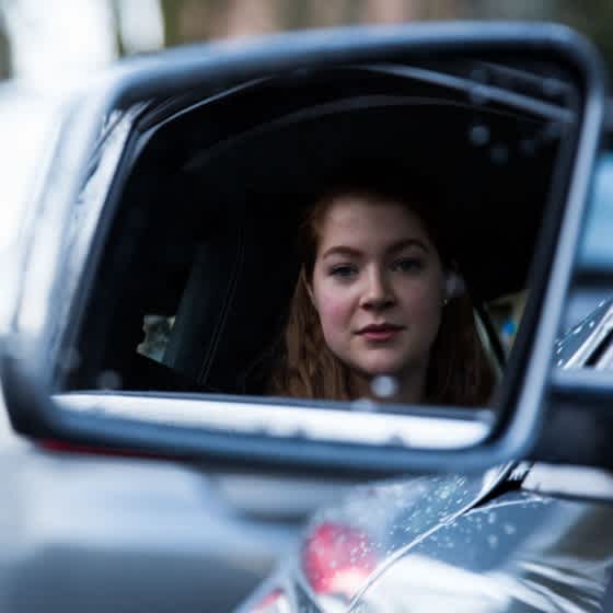 die Fahranfängerin Lucy im Seitenspiegel eines Autos.