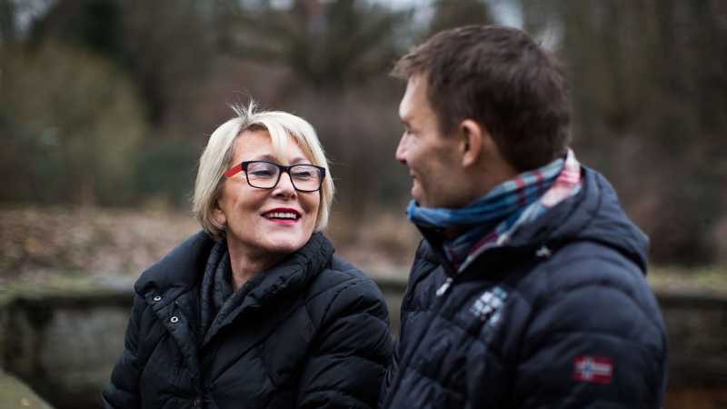 René Heinen und seine Mutter sitzen draußen nebeneinander und unterhalten sich.