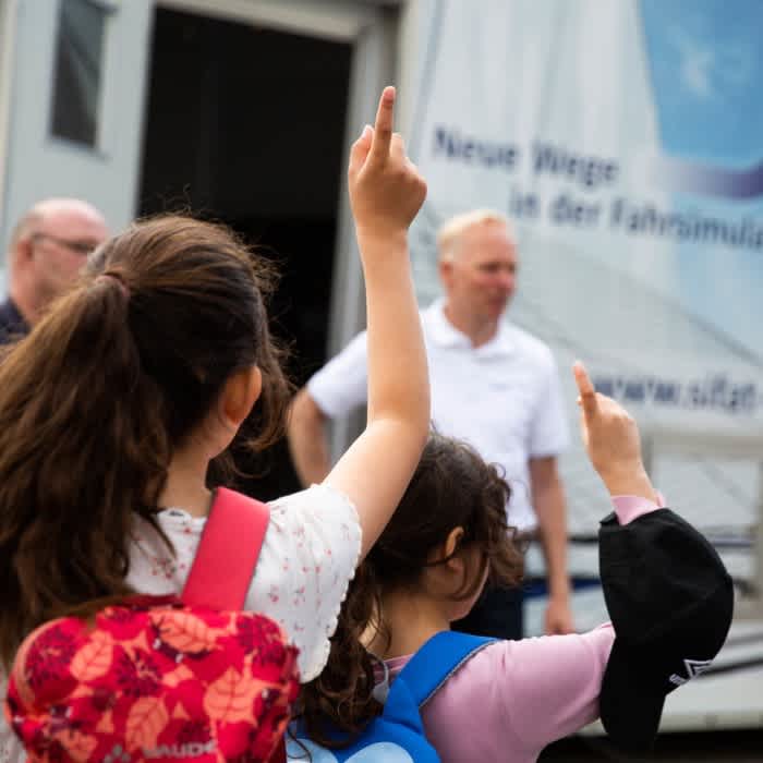 Eine kleine Gruppe von Schülerinnen meldet sich. Dahinter ist ein Container zu sehen, darin befindet sich ein Lkw-Simulator.  