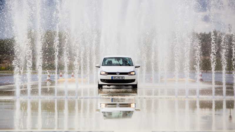 Ein weißes Auto fährt durch eine Wasserfontäne. 