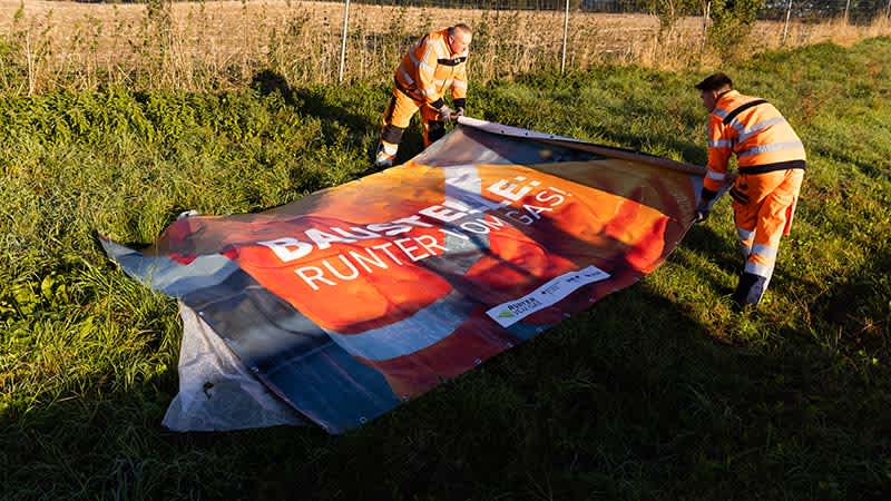 Zwei Straßenwärter rollen ein Autobahnplakat auf dem Boden aus.