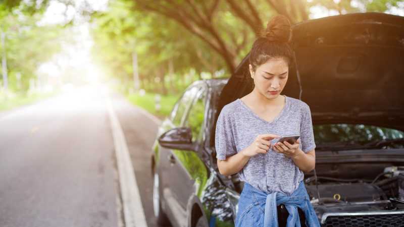 Eine Frau vor einer geöffneten Motorhaube und bedient ihr Handy.