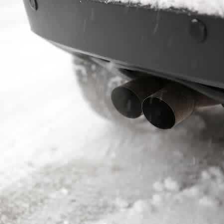 Das Bild zeigt den Auspuff eines Autos über einer verschneiten Straße.