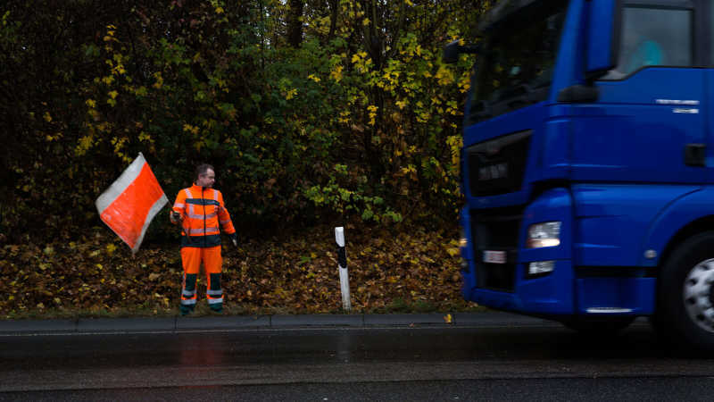 Ein Straßenwärter schwenkt eine orangene Fahne, um einen LKW-Fahrer auf sich aufmerksam zu machen.