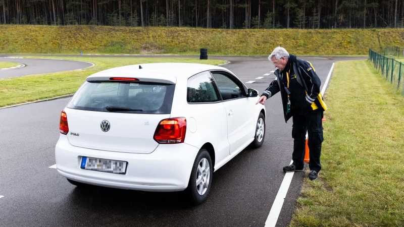 Ein Fahrtrainer steht an einem weißen Auto und gibt Hilfestellung beim Einparken. 