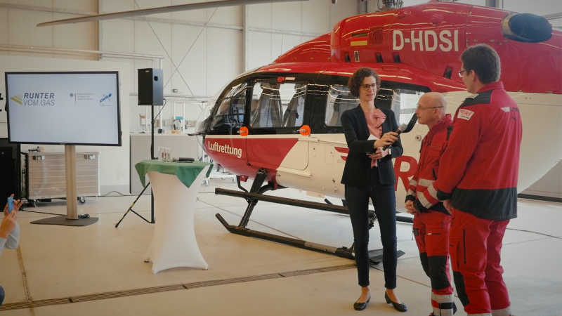 zwei Rettungskräfte sprechen vor einem Rettungshubschrauber ins Mikrofon auf der Pressekonferenz zu den neuen Autobahnplakaten 2017.