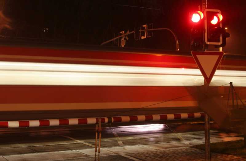 Man sieht einen Zug, der nachts an einem Bahnübergang vorbeifährt.