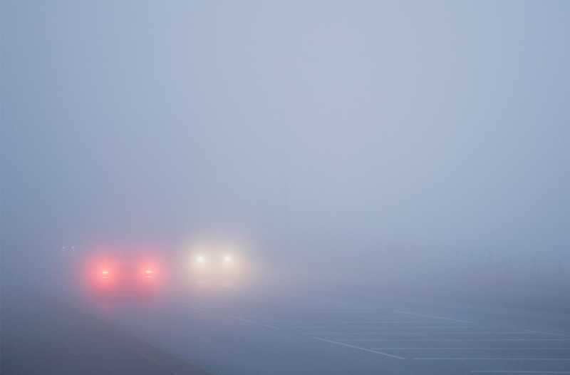 Das Bild zeigt die Vorderlichter eines und die Rücklichter eines anderen Autos im Nebel auf einer Straße.