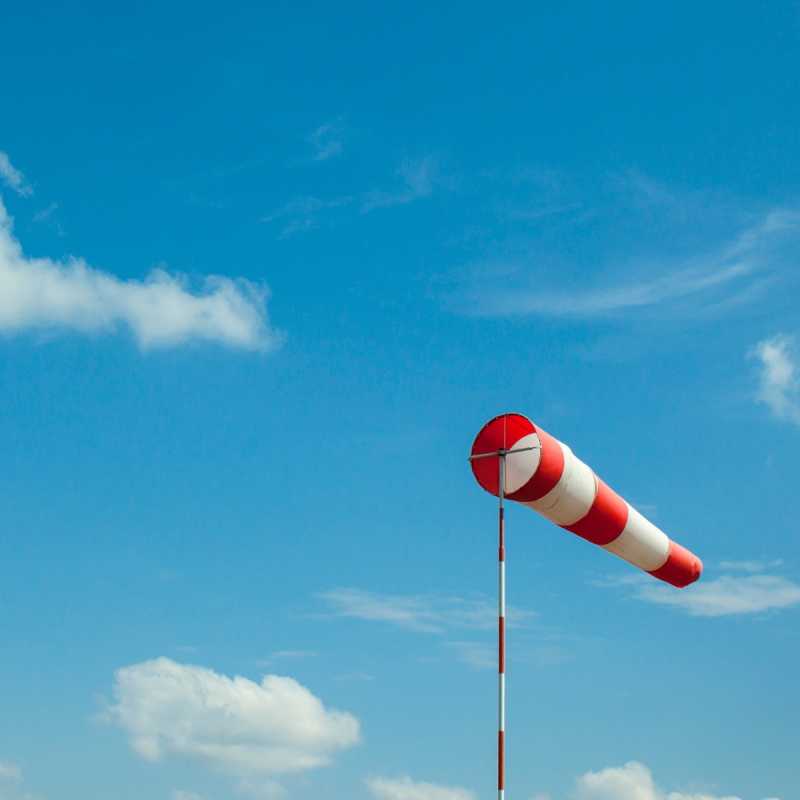 Das Bild zeigt einen rot-weiß gestreiften Windsack vor blauem Himmel.