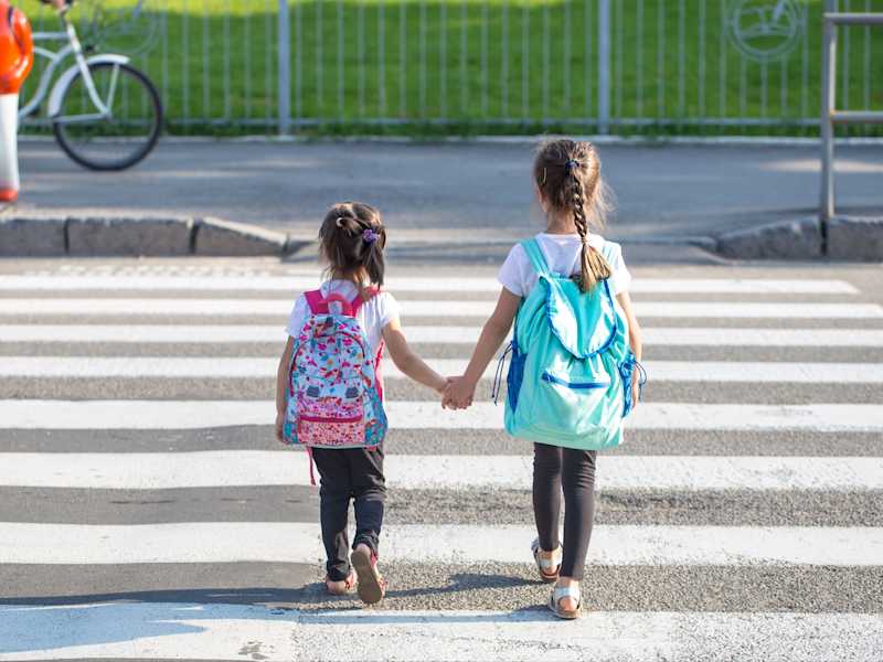 Zwei Kinder überqueren gemeinsam einen Zebrastreifen.