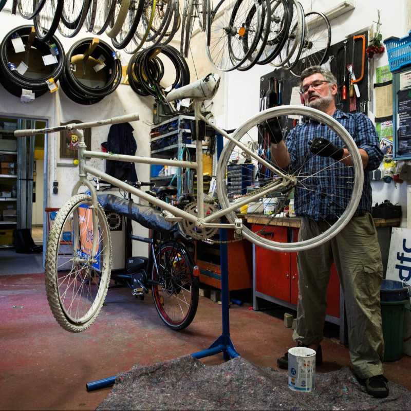 Der Fahrradhändler steht vor einem weißen Fahrrad in seinem Fahrradladen und streicht die letzten Stellen.