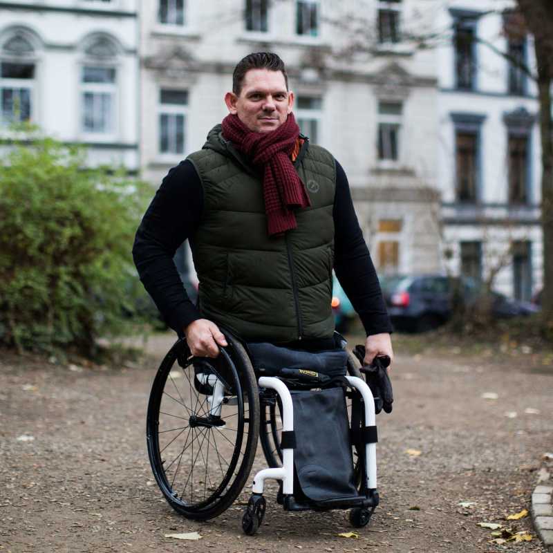 Man sieht einen Mann ohne Beine im Rollstuhl sitzen und lächeln.