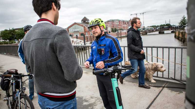 Der Fahrradpolizist Jens Cissek schreibt einem E-Scooter-Fahrer ein Ticket auf einer Brücke in Hamburg.