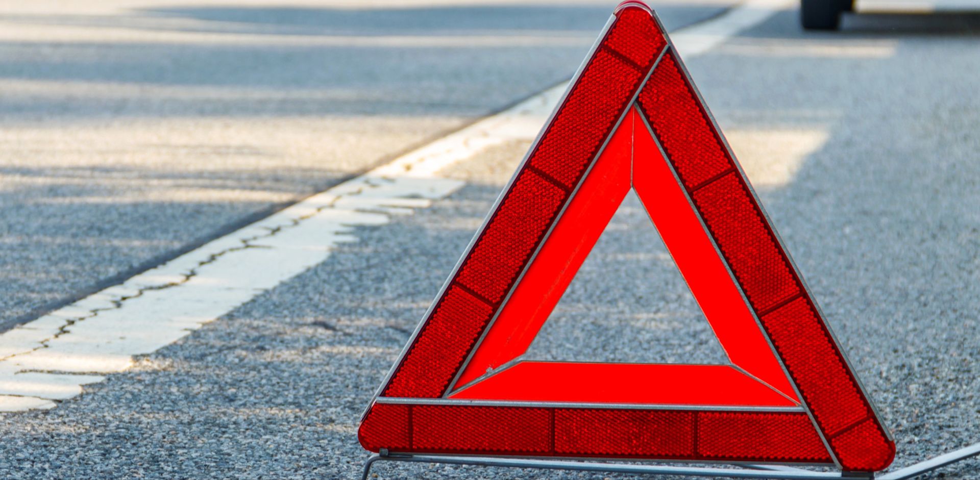 Rotes Warndreieck auf dem Asphalt am Seitenstreifen. Das Warndreieck sichert eine Pannen- oder Unfallstelle ab und warnt den Verkehr. 
