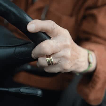 Man sieht die Hände einer älteren Dame, die das Steuer eines Autos umgreifen.