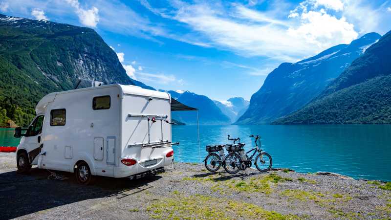 Das Bild zeigt einen Wohnwagen und zwei Fahrräder am Ufer eines Sees.