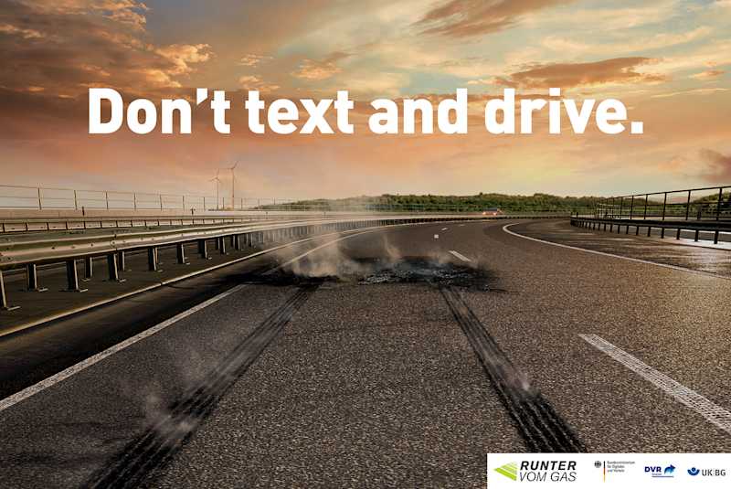 Ein Plakat zeigt eine dampfende Autobahn nach einer Vollbremsung . Ein Schriftzug schreibt: Don't text and drive. 