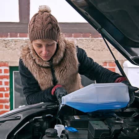 Eine Frau füllt das Frostschutzmittel ihres Autos nach.