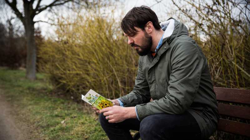 Das Bild zeigt einen jungen Mann auf einer Parkbank, der eine Dankeskarte liest.