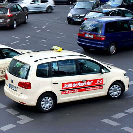 zwei Taxis fahren über eine Kreuzung hinter weiteren Autos.