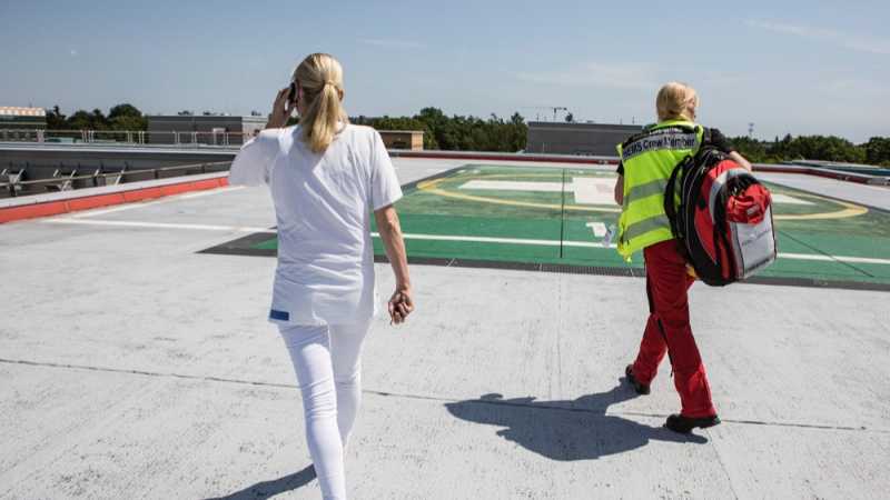 Das Bild zeigt eine Ärztin und eine Sanitäterin auf dem Dach eines Krankenhauses, auf dem ein Hubschrauberlandeplatz zu sehen ist. 