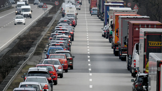 Stau auf einer zweistreifigen Autobahn mit einer langen Schlange von Autos links und einer Kolonne von Lastwagen und Fahrzeugen auf der rechten Spur.
