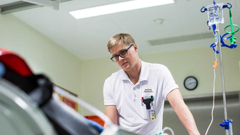 Florian Kunz sieht auf einen Patienten auf einem Krankenhausbett herab.