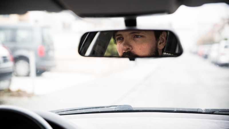 Das Bild zeit die Nahaufnahme eines Autorückspiegels während der Fahrt. Darin zu sehen: Der auf die Straße gerichtete Blick von Marius Nolte.