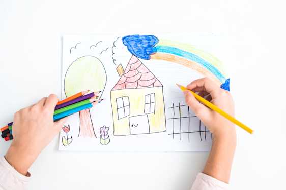 Manos de niño dibujando con colores una casa