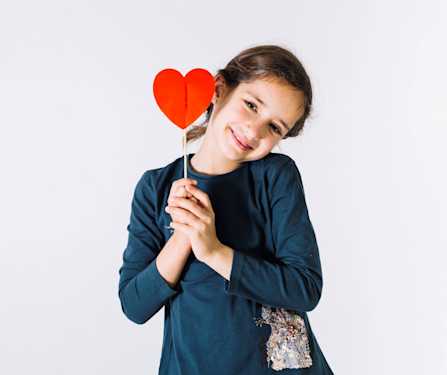 niña sujetando un corazón de cartulina en sus manos y sonriendo