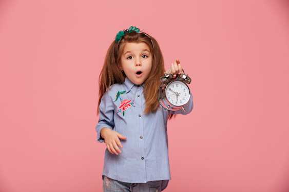 niña con cara de asombro con un reloj despertador en la mano