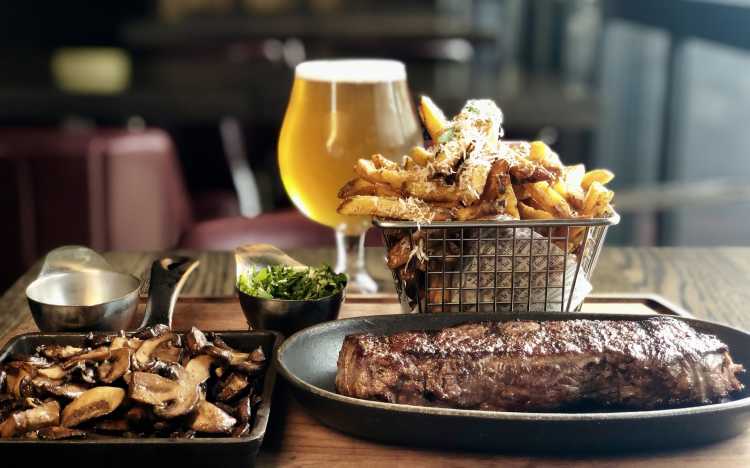 A steak with fries, fixings, and beer served at The Commoner Roncy.