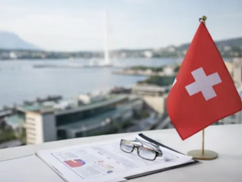 Drapeau suisse posé sur un bureau avec documents financiers et vue sur Genève