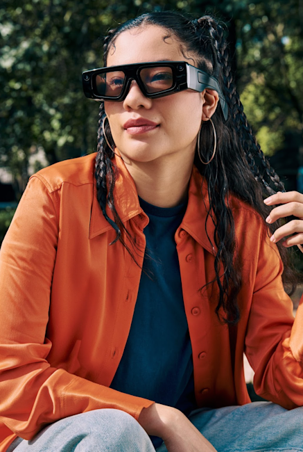 Photo of a woman wearing the new Spectacles in front of green, vibrant scenery.