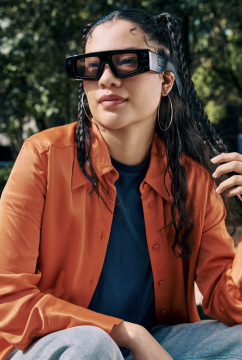 Photo of a woman wearing the new Spectacles in front of green, vibrant scenery.