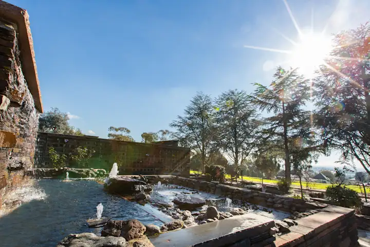 Water fountains and pool of water at Templestowe Cemetery amongst a blue sky and tall trees