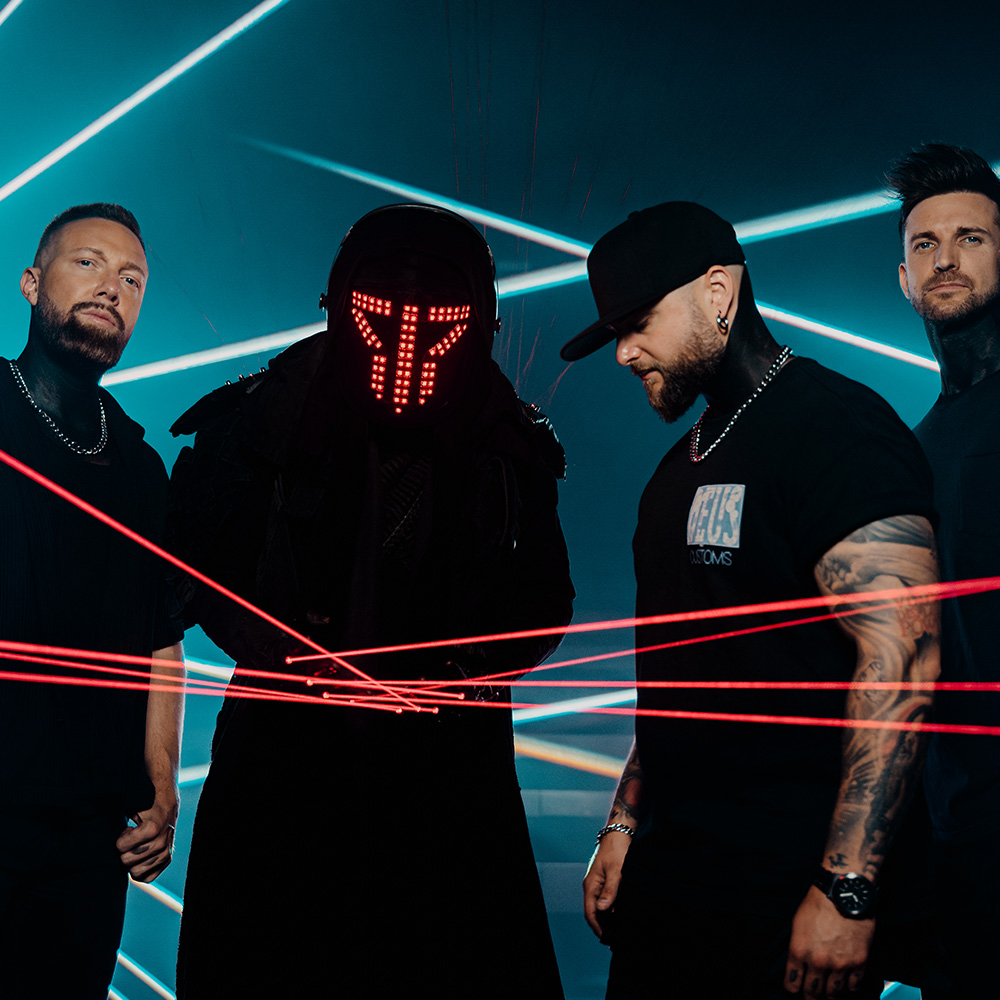 Fyra män, varav en bär en upplyst mask och mörk mantel, står bland röda laserstrålar i en mörk, rökig miljö med blå laserljus i bakgrunden.