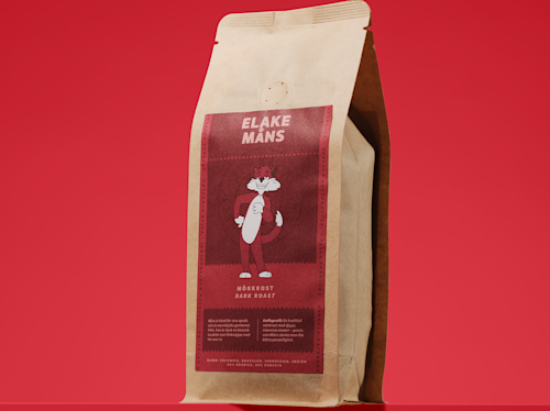 A brown paper bag of coffee labeled "Eläke Mäns," featuring an illustrated cat in the center on a red background, with text describing it as a dark roast.