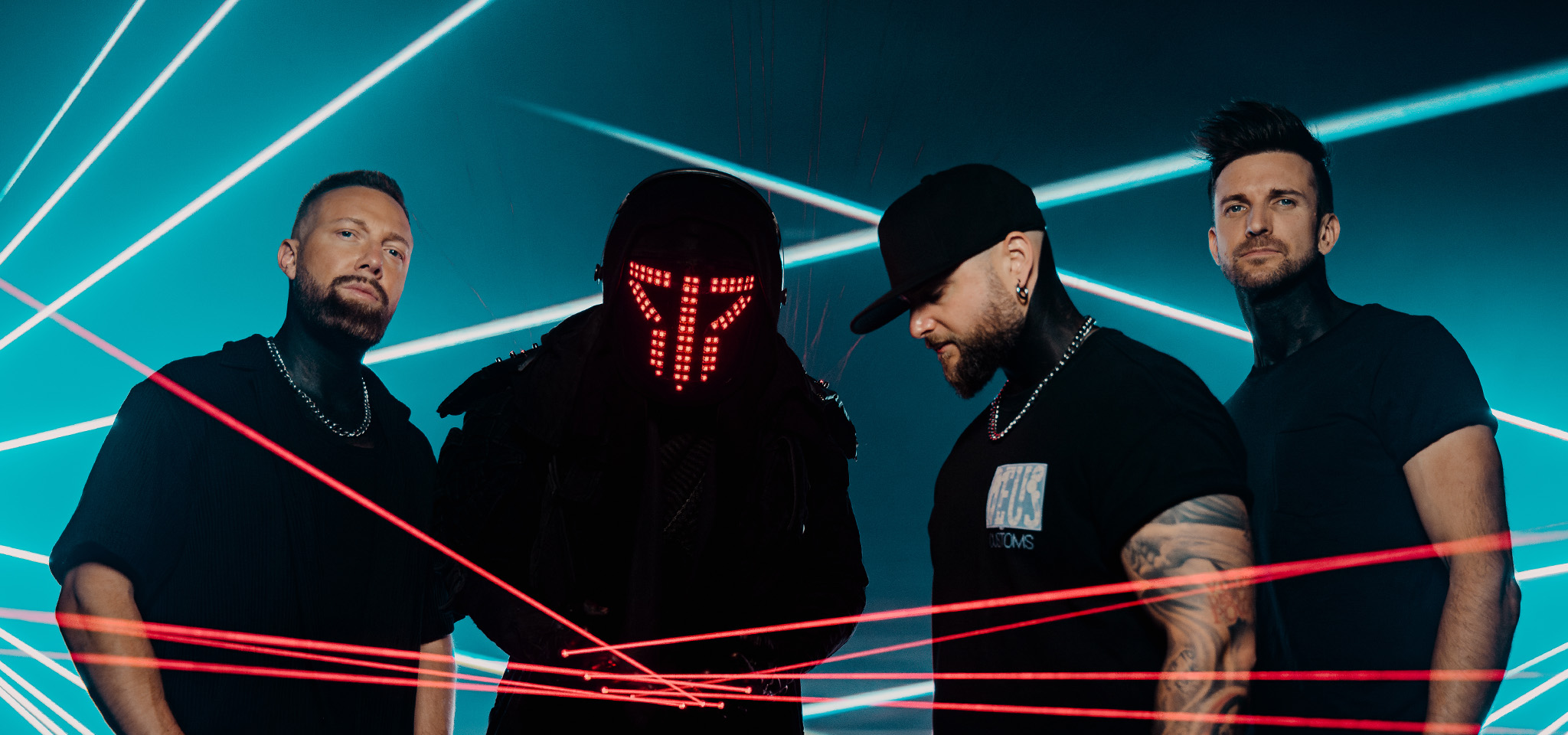Fyra män står mitt bland röda laserstrålar och blått ljus; en bär en futuristisk hjälm med röda LED-lampor, medan de andra bär svarta skjortor och hattar.